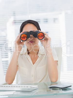 Businesswoman looking through binoculars at desk