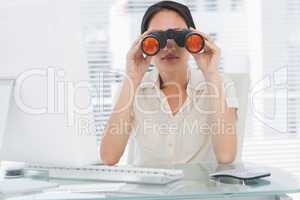 Businesswoman looking through binoculars at desk