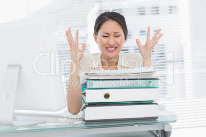 Angry businesswoman shouting with stack of folders at desk