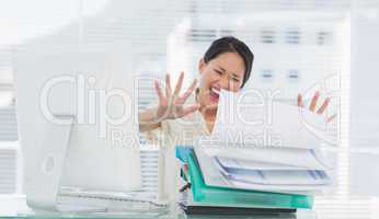 Businesswoman shouting with stack of folders at desk
