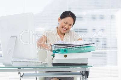 Angry businesswoman with stack of folders at desk