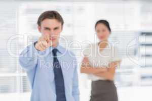 Businessman pointing towards camera with woman in office