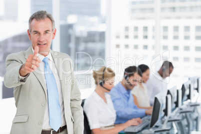 Businessman gesturing thumbs up with executives using computers Businessman gesturing thumbs up with executives using computers