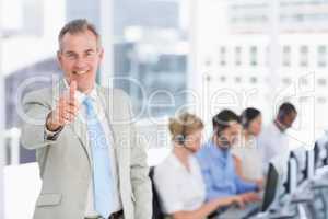 Businessman gesturing thumbs up with executives using computers