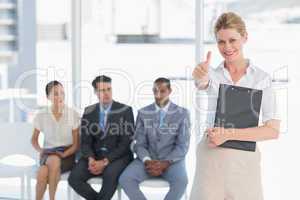 Woman gesturing thumbs up with people waiting for interview in o