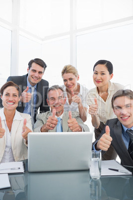 Business colleagues with laptop gesturing thumbs up at desk