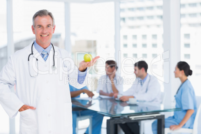 Doctor holding apple with group around table at hospital