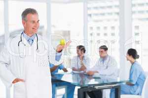 Doctor holding apple with group around table at hospital