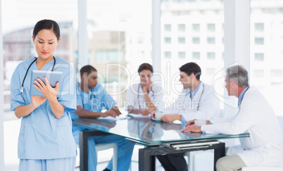 Surgeon using digital tablet with group around table in hospital