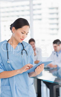 Surgeon using digital tablet with group around table in hospital