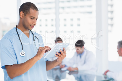 Surgeon using digital tablet with group around table in hospital