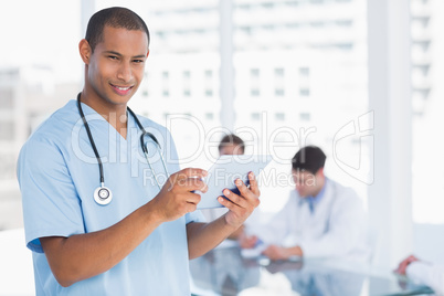 Murgeon using digital tablet with group around table in hospital