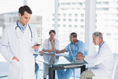 Doctor text messaging with group around table in hospital