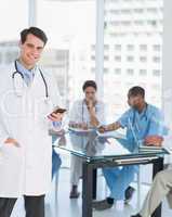 Doctor text messaging with group around table in hospital