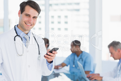 Doctor text messaging with group around table in hospital