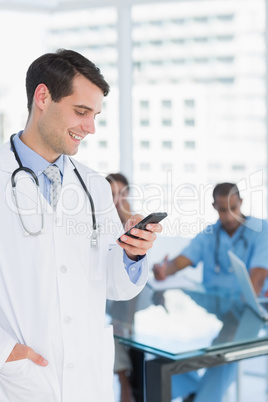 Doctor text messaging with group around table in hospital