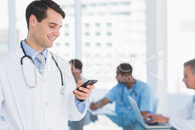 Doctor text messaging with group around table in hospital