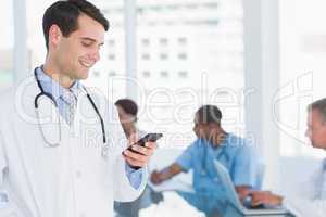 Doctor text messaging with group around table in hospital