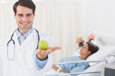 Smiling doctor holding apple with patient in hospital