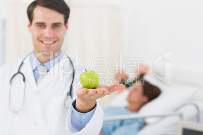 Smiling doctor holding apple with patient in hospital