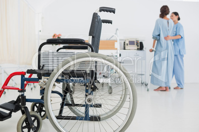 Doctor helping patient to walk with wheelchair in foreground