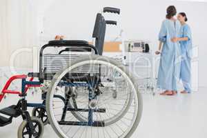 Doctor helping patient to walk with wheelchair in foreground