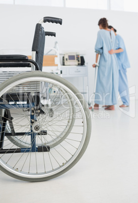 Doctor helping patient to walk with wheelchair in foreground