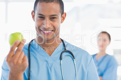 Male surgeon holding an apple with colleague behind