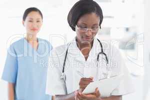 Female doctor writing report with surgeon in background