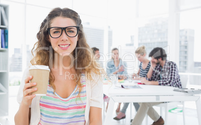 Woman holding disposable coffee cup with colleagues in backgroun