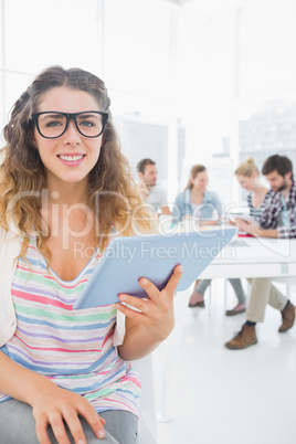 Woman using digital tablet with colleagues in background at offi
