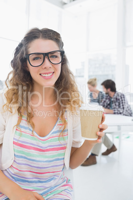 Woman holding disposable coffee cup with colleagues in backgroun