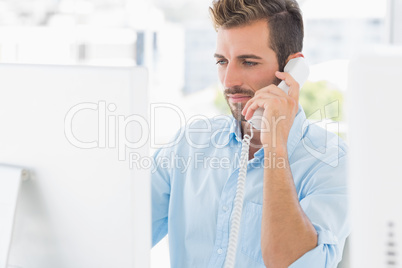 Serious man using phone and computer in office