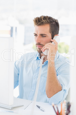 Serious man using phone and computer in office