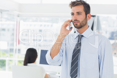 Casual male artist using mobile phone with colleague in the back