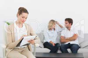 Financial adviser writing notes with couple in background