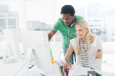 Artist drawing something on paper with colleague at office