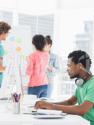 Casual man using computer with colleagues behind in office