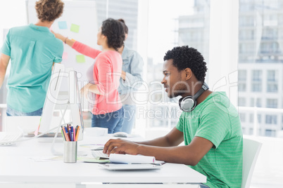 Casual man using computer with group of colleagues behind in off