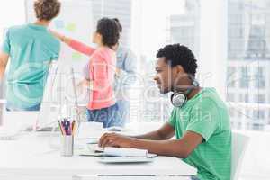 Casual man using computer with group of colleagues behind in off