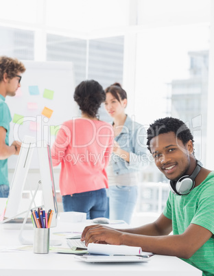 Casual man using computer with colleagues behind in office