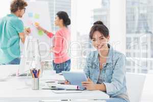 Casual woman using digital tablet with colleagues behind in offi