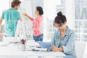 Casual woman using digital tablet with colleagues behind in offi