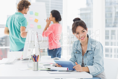 Casual woman using digital tablet with colleagues behind in offi