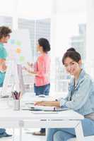 Casual woman using computer with colleagues behind in office