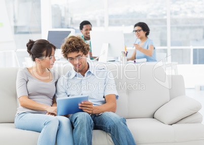 Casual couple using digital tablet with colleagues at creative o