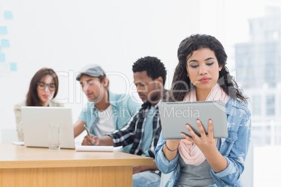 Concentrated woman using digital tablet with colleagues behind i