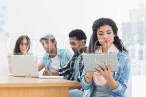 Concentrated woman using digital tablet with colleagues behind i