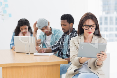 Concentrated woman using digital tablet with colleagues behind i