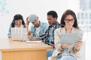 Concentrated woman using digital tablet with colleagues behind i